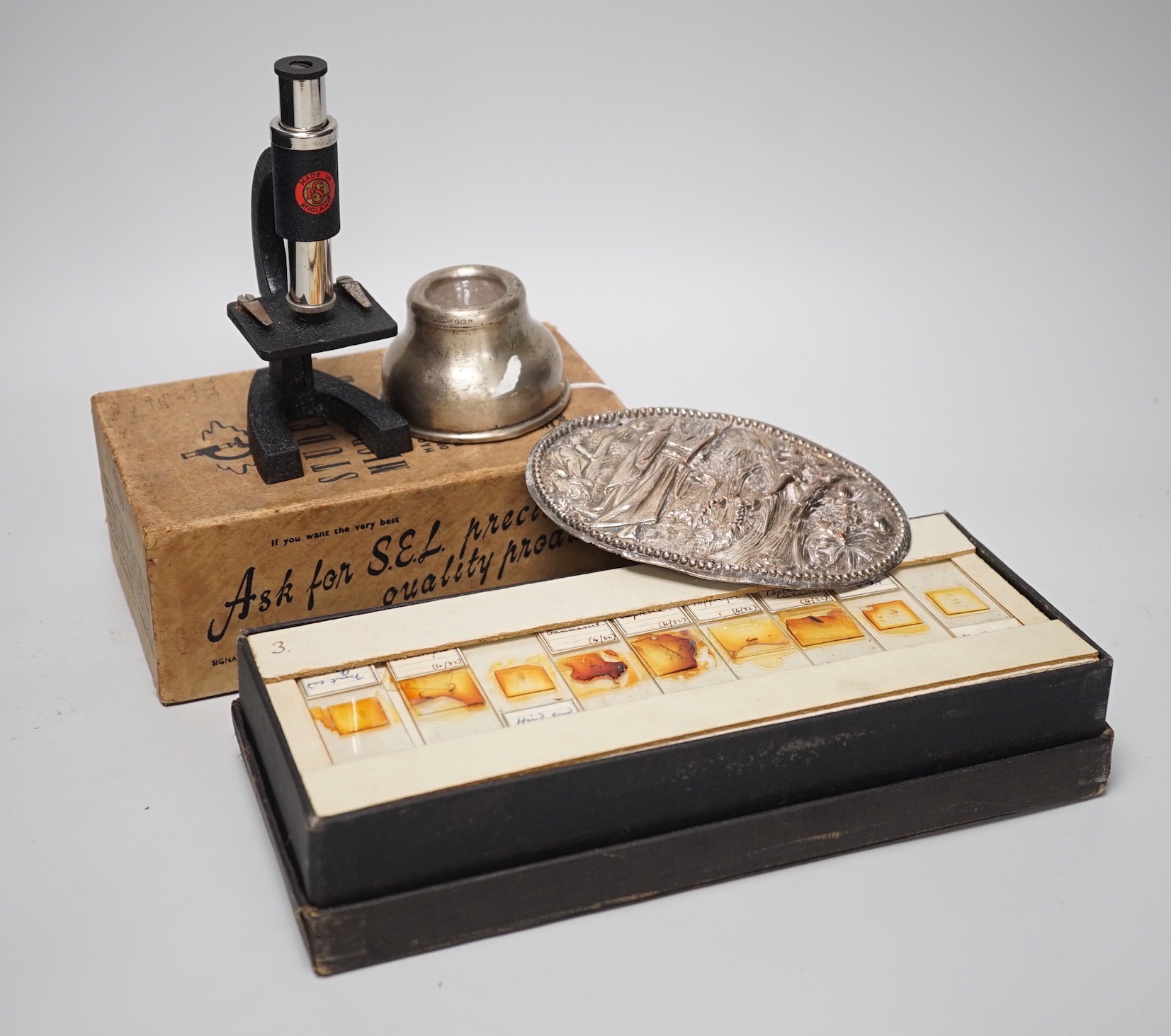 A case of early 20th century microscopes slides and a student's microscope, a small silver inkwell and a small plated figural plaque